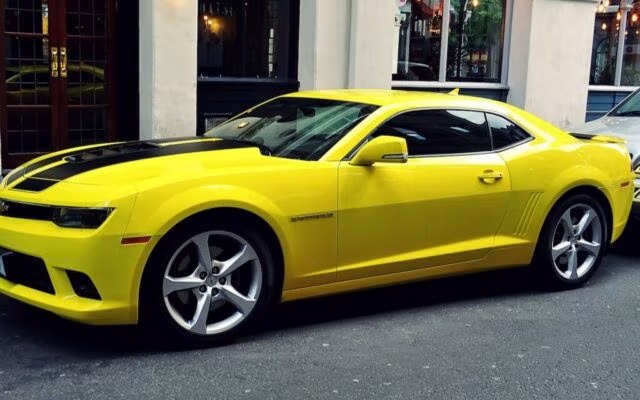 Żółty Chevrolet Camaro zaparkowany przy miejskiej ulicy przed eleganckim budynkiem